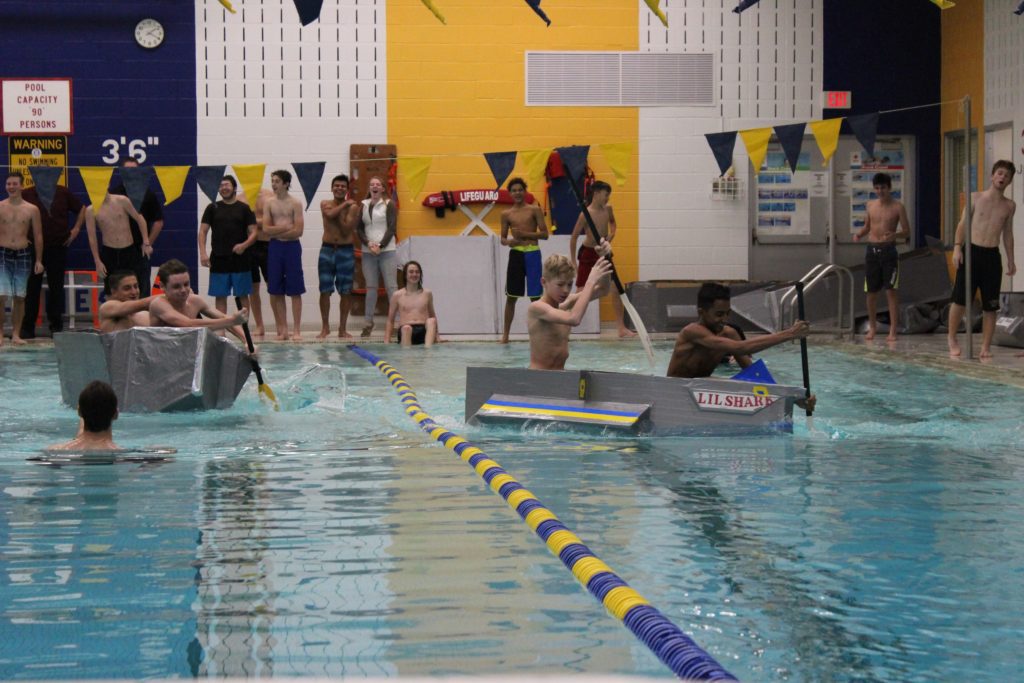 Students in pool paddling boats made of cardboard and duct tape