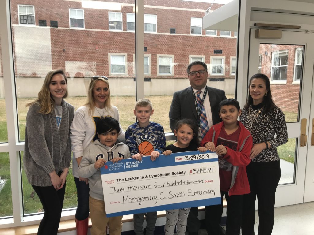 adults and elementary students holding a big check