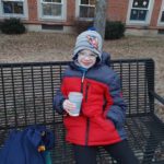 an elementary student seated on a bench enjoying hot cocoa