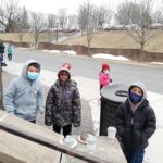 a group of elementary students outdoors enjoying donuts and hot cocoa