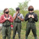 three high school students wearing waders by the river