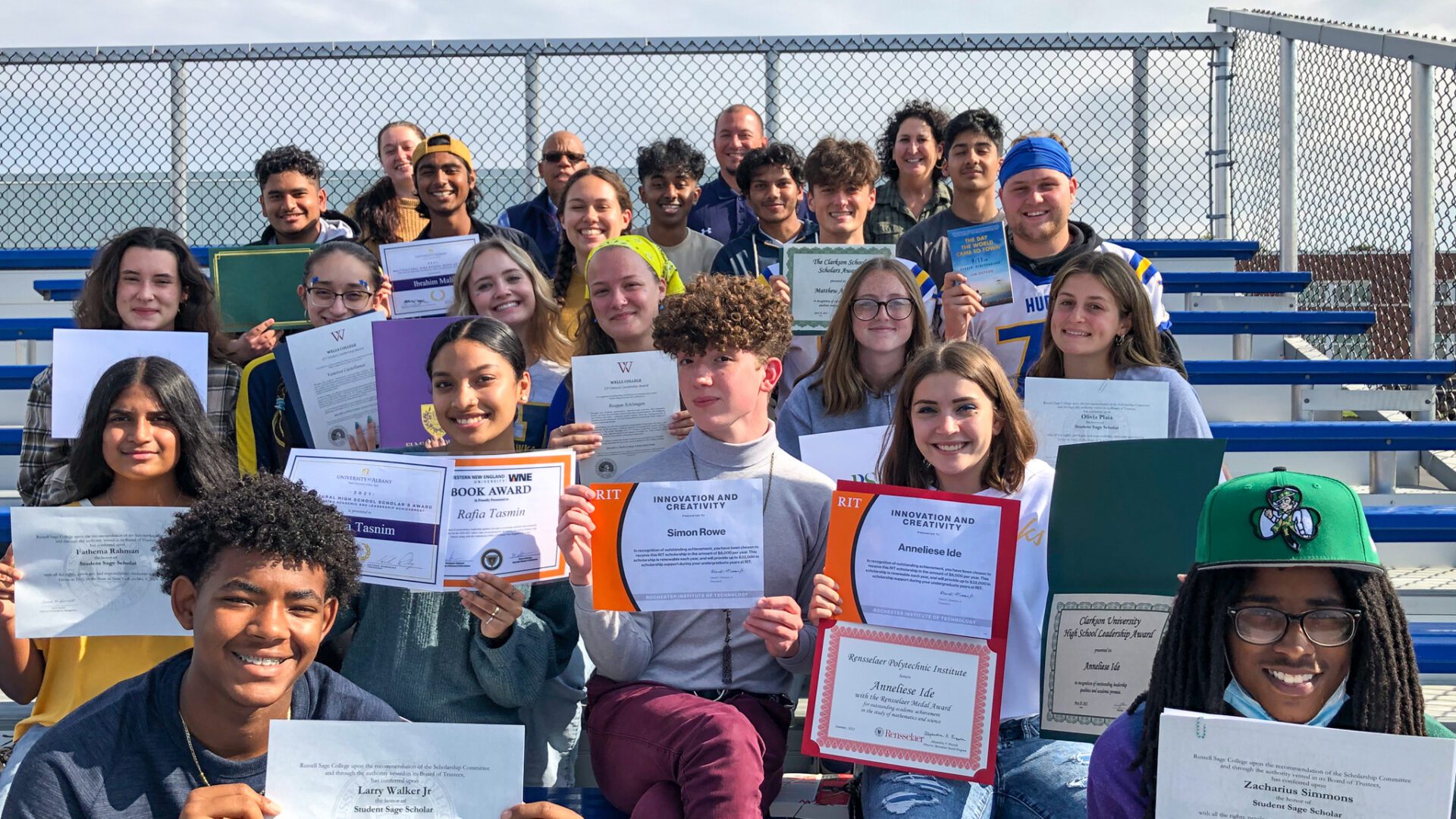 a group of high school students holding up certificates while seated on outdoor bleachers