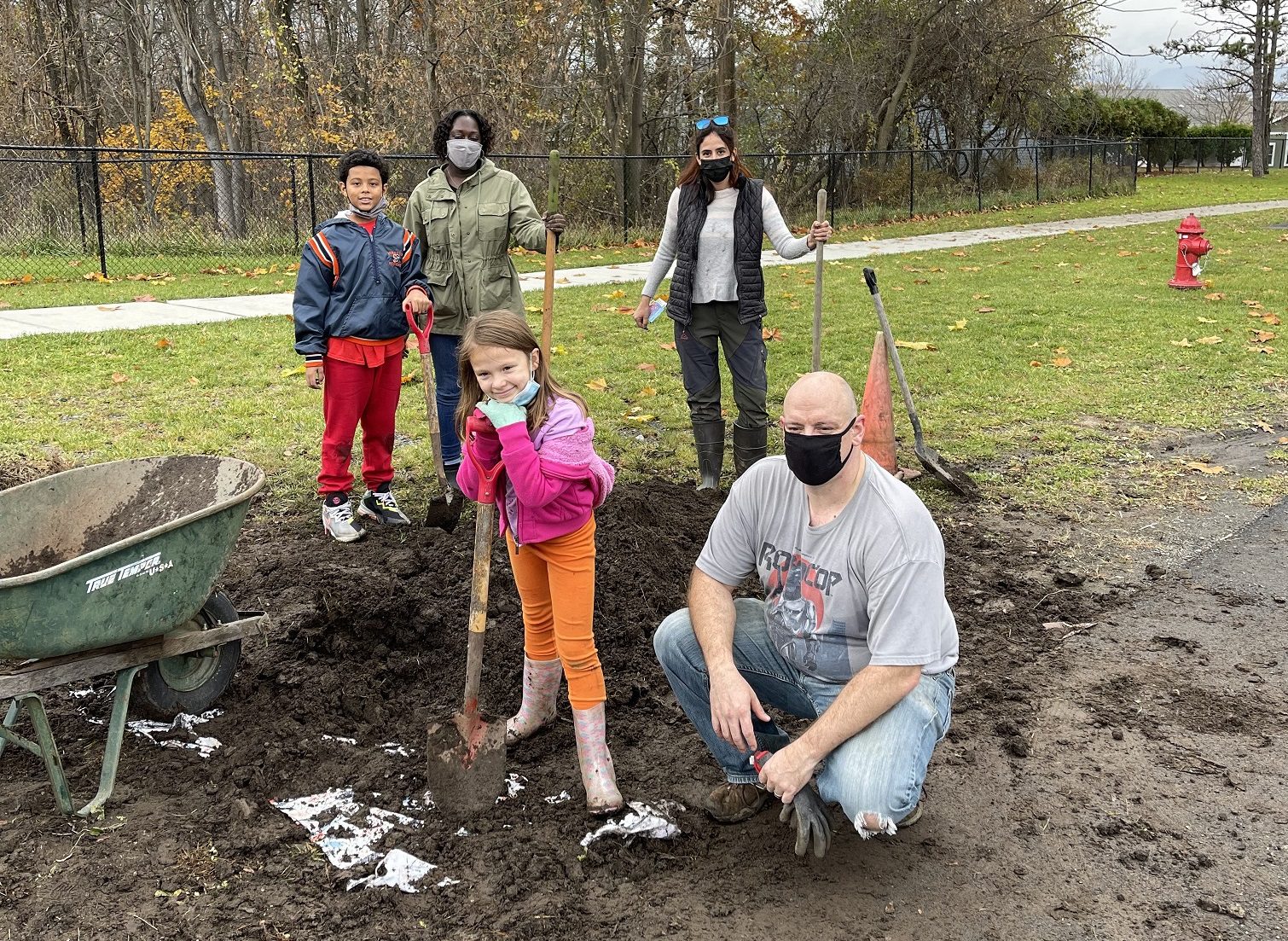 two elementary students and three adults outside in a dirt patch with shovels