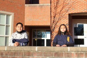 a boy and girl smiling in front of the school