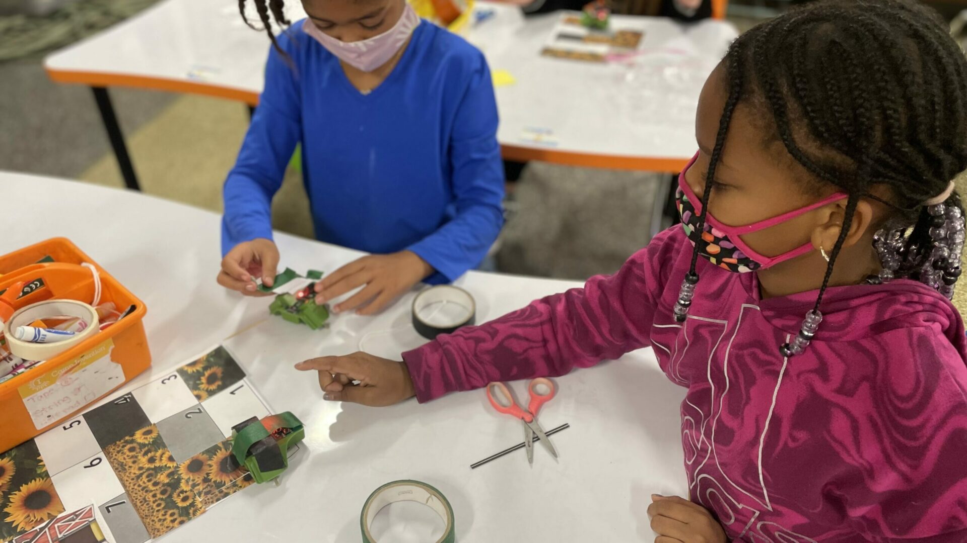 two young African American girls at a table work on a pollination activity