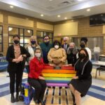 a group of masked school leaders around a rainbow bench in the cafeteri