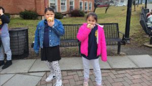 two elementary school girls eating breakfast pastries on the back school patio
